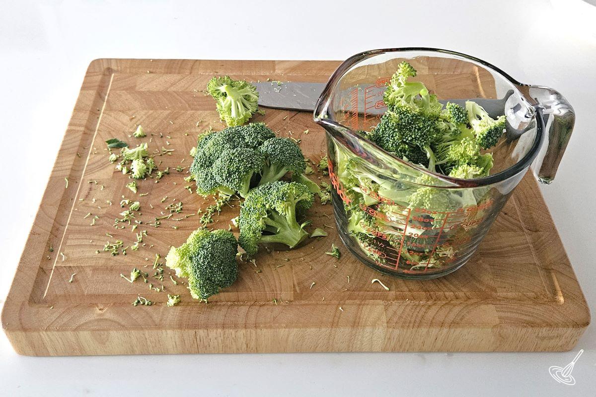 Someone chopping broccoli florets on a wooden cutting board. 