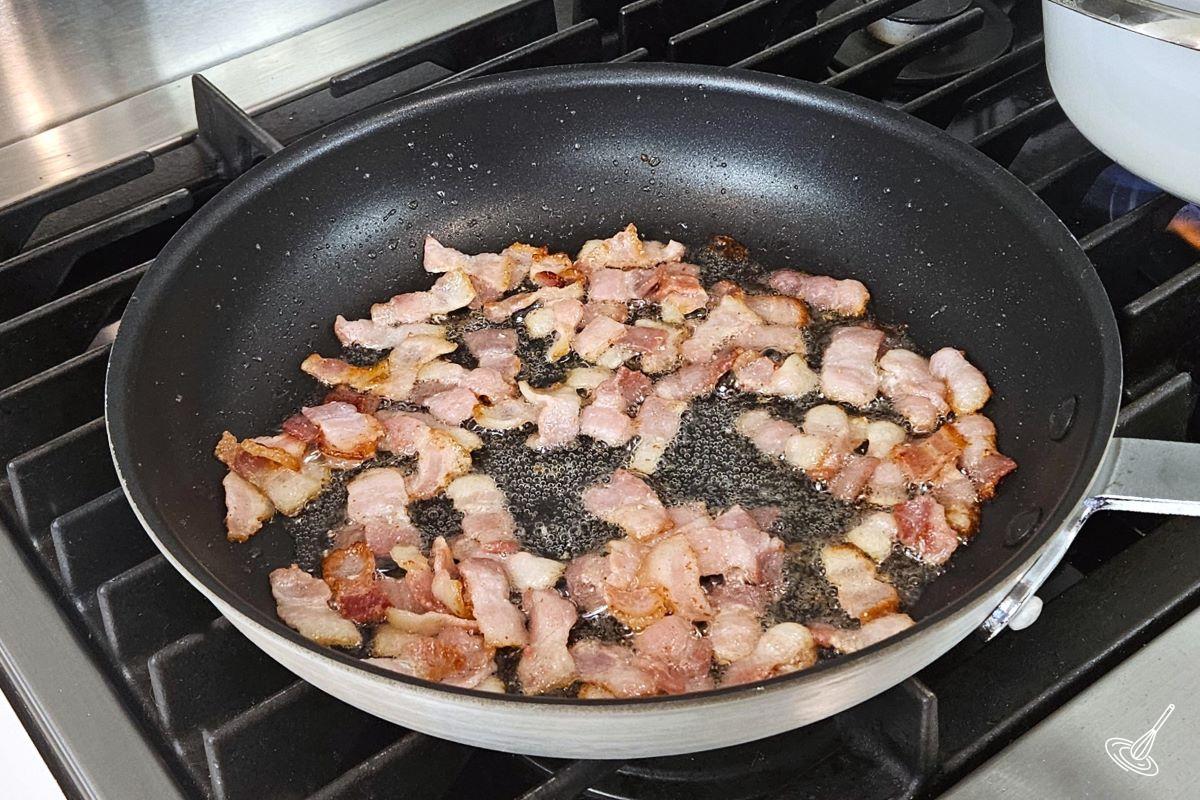 Chopped bacon cooking in a large frying pan.