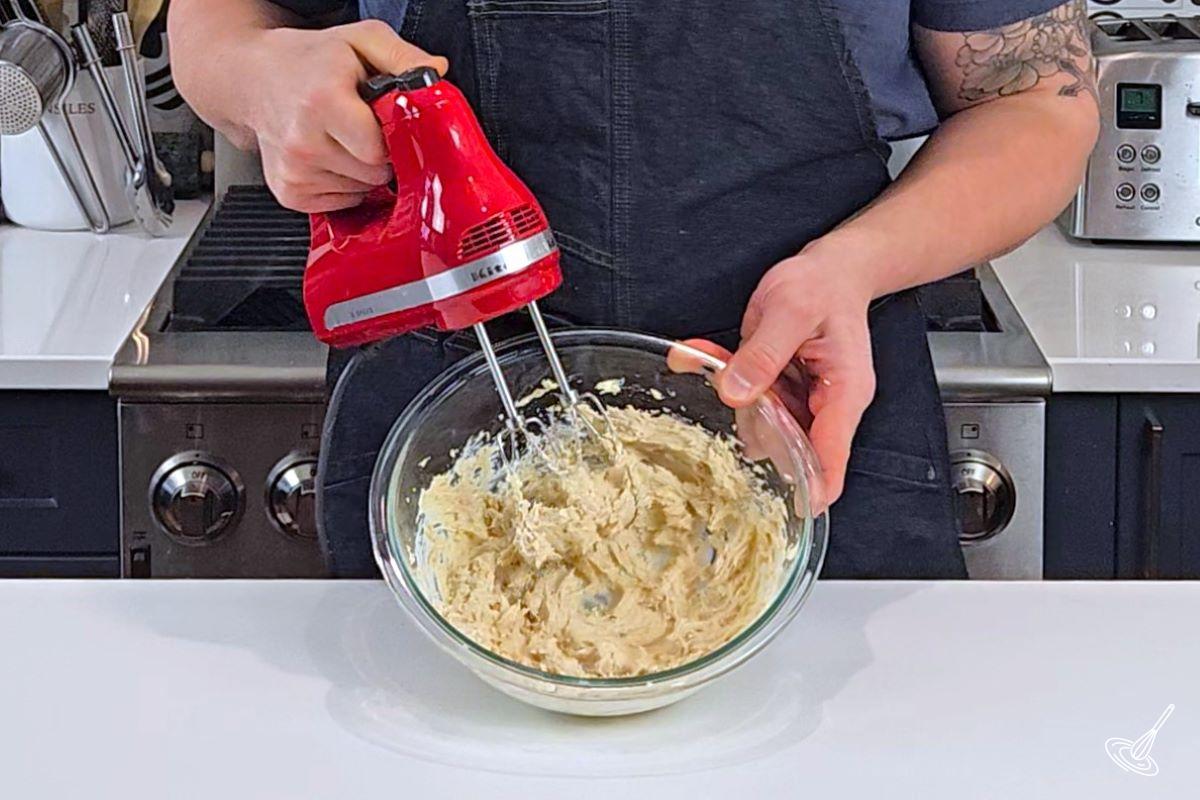 Someone using a hand blender to mix butter and sugar. 