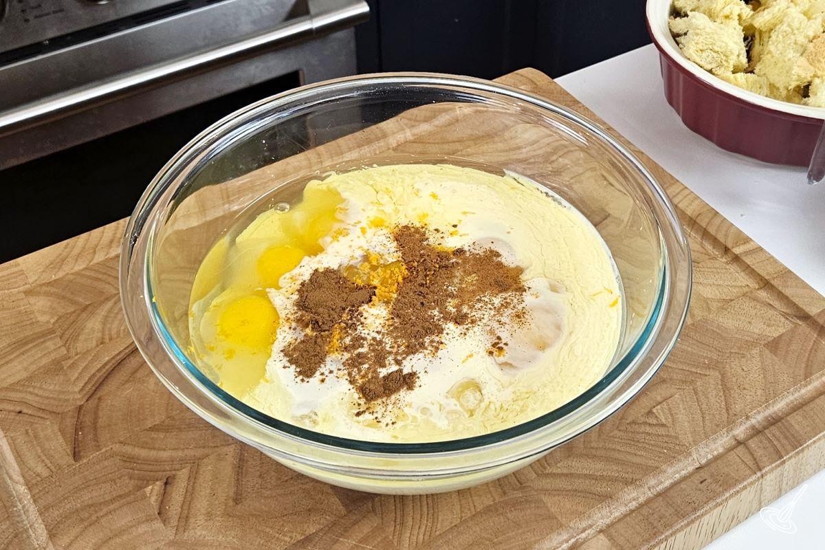 A large bowl containing eggnog, eggs, cinnamon, orange zest and vanilla.