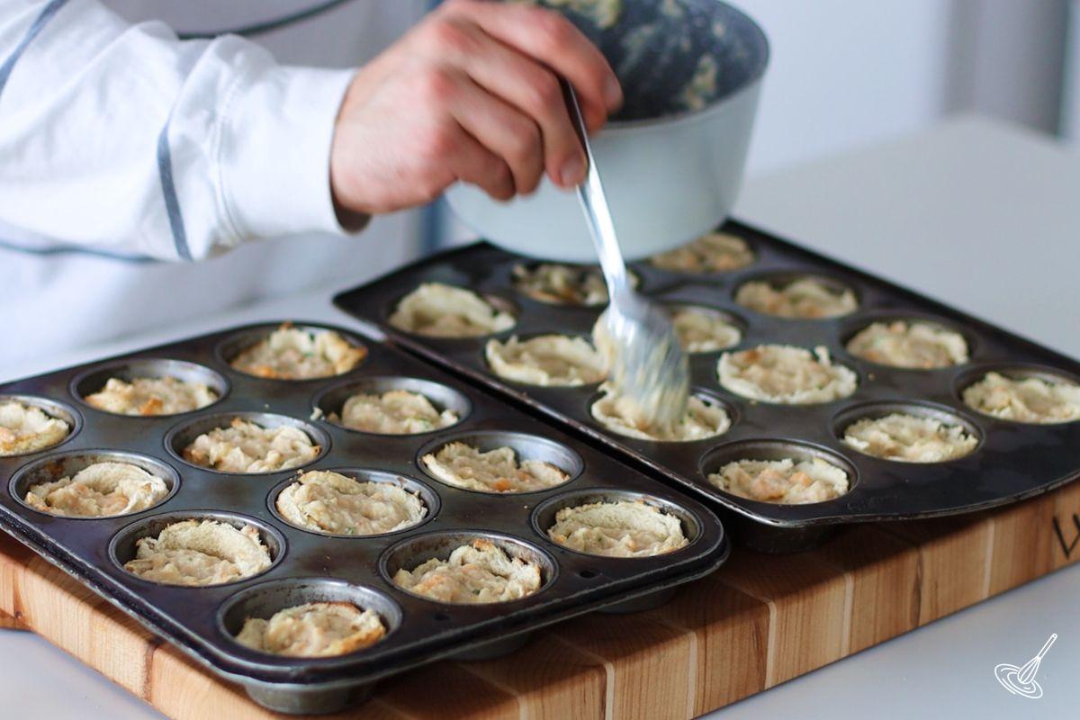 Someone placing a tablespoon of crab puffs mixture into the bread shells.