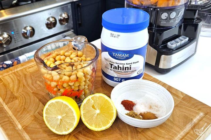 Chickpeas, tahini, lemon and spices on a cutting board.