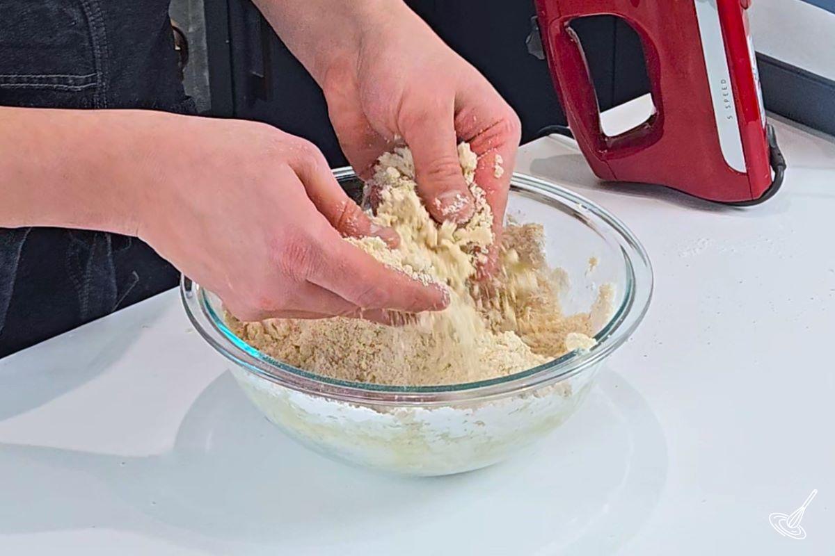 Someone using their hand to mix flour and butter to make a crumble.