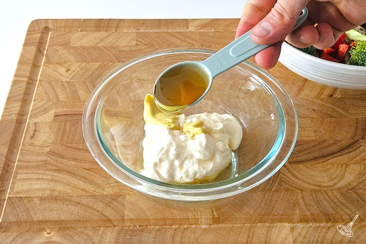 Someone adding liquid honey to a small bowl with mayonnaise to make salad dressing. 
