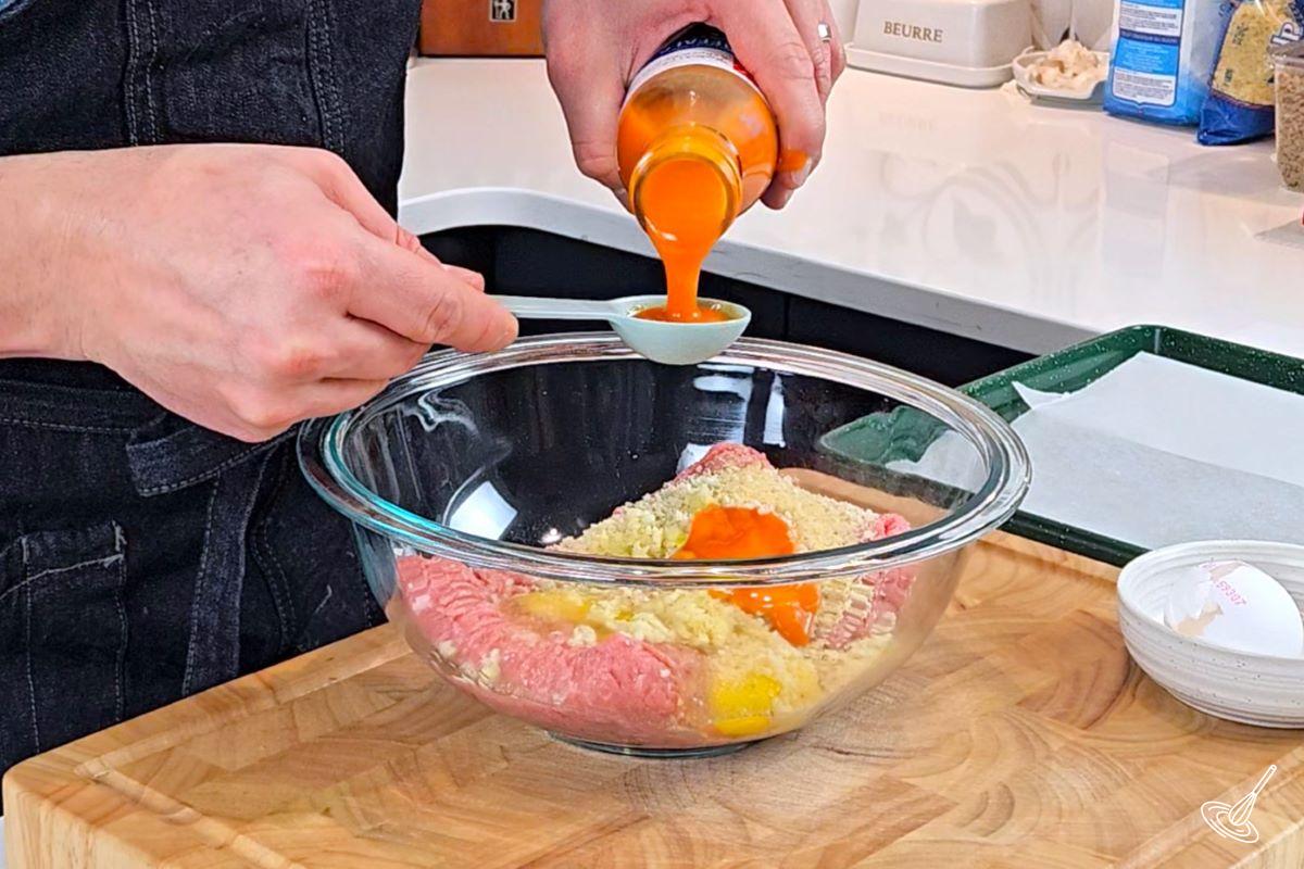 Someone pouring buffalo sauce in a large bowl with ground turkey.