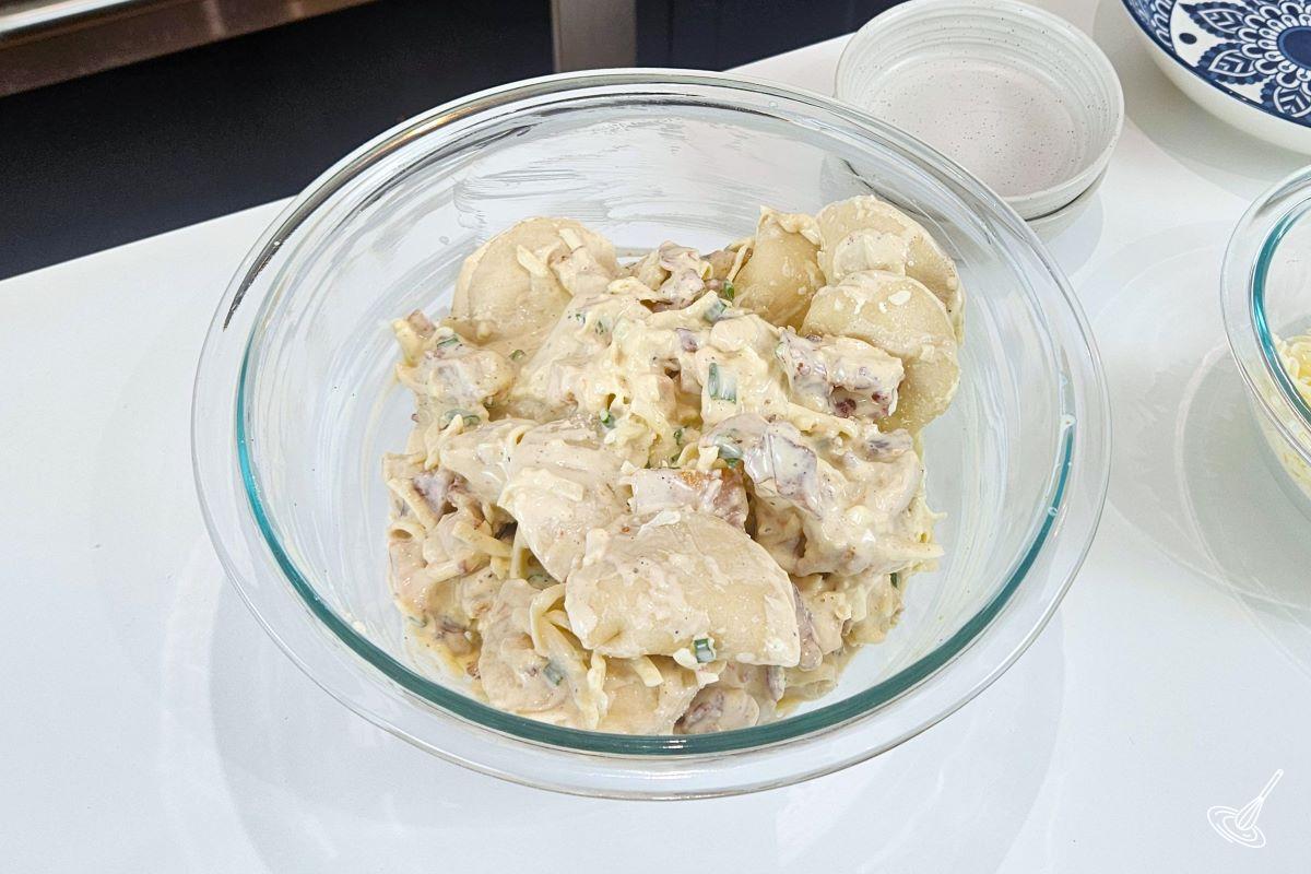 A large bowl containing pierogies, green onion, bacon bits, cheese, and ranch dressing. 