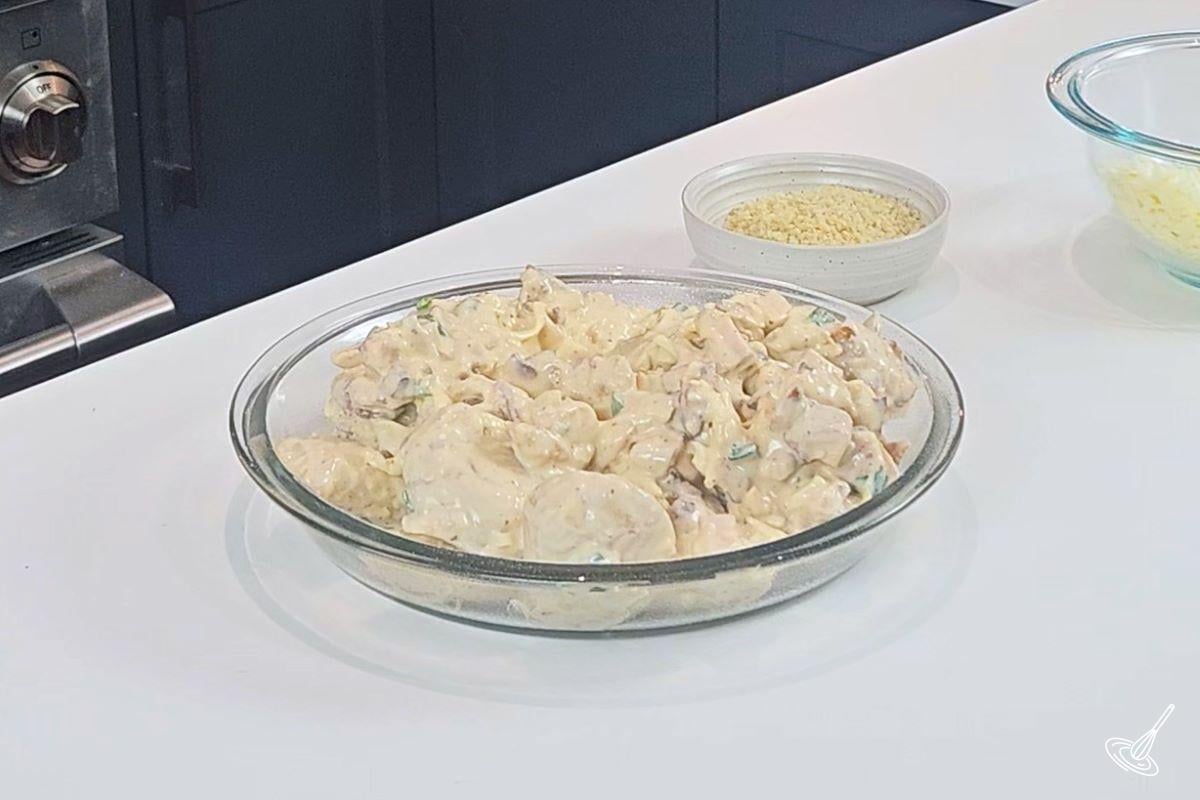 Pierogies, green onion, bacon bits, cheese, and ranch dressing mixture, in a pie plate.