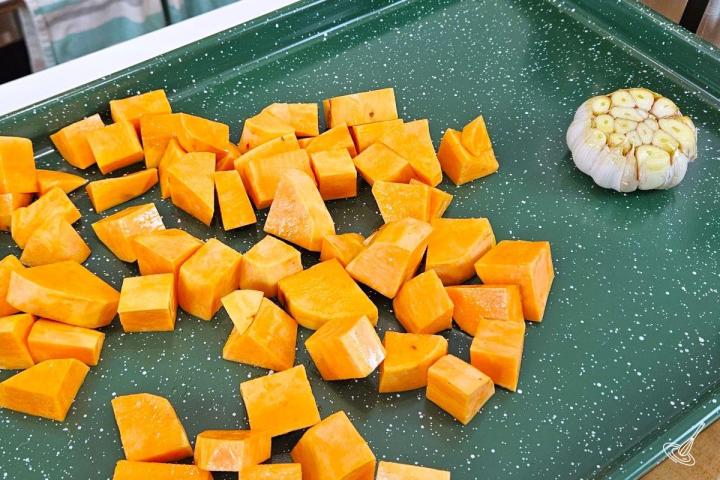 Cubes of sweet potato and a bulb of garlic on a baking tray. 