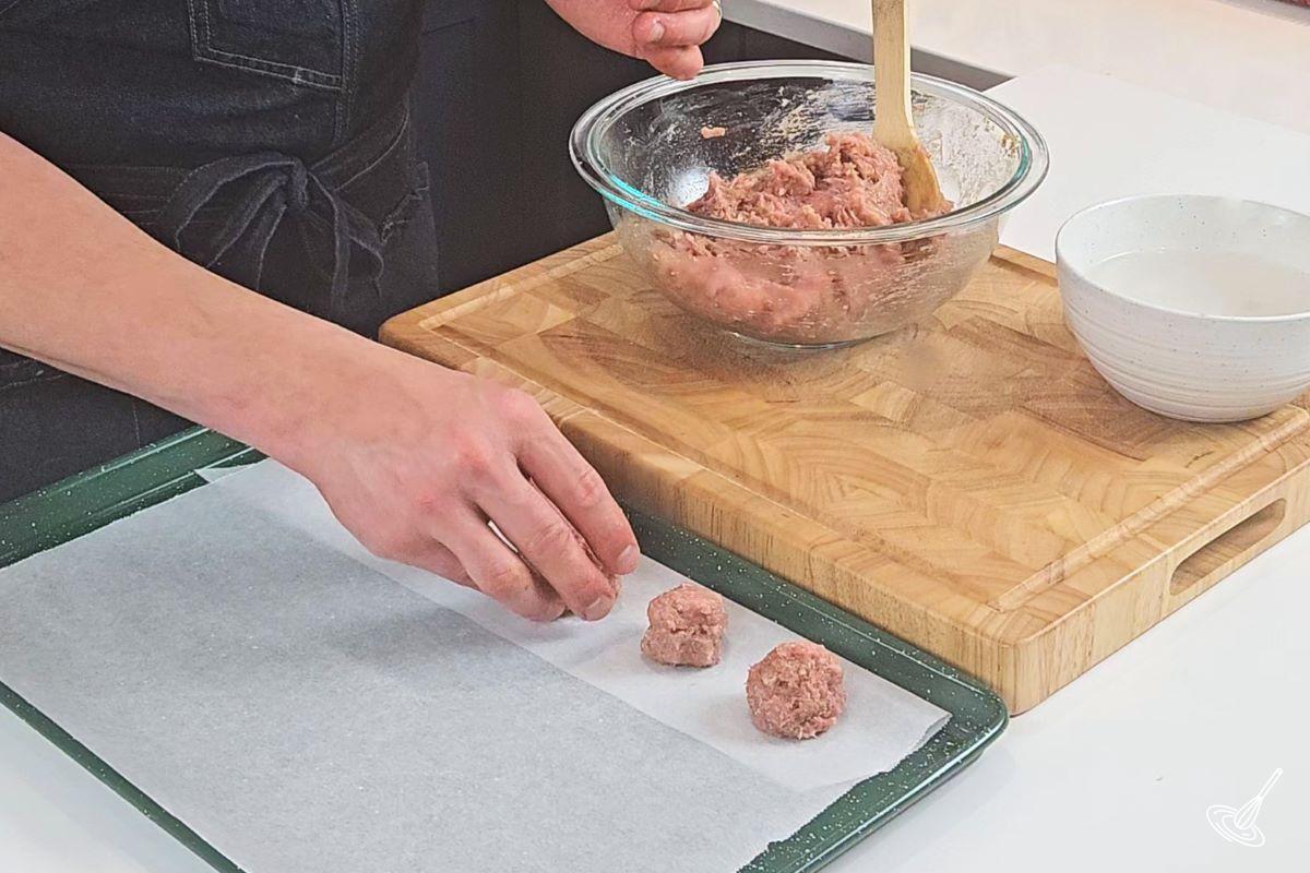 Someone shaping meatballs and placing them on a baking tray.