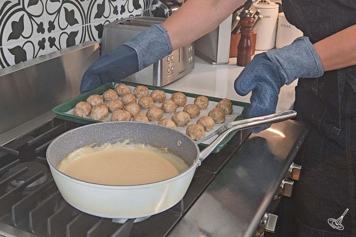 Someone taking a tray of meatballs out of the oven. 