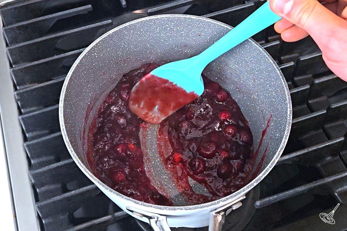 Someone stirring a sauce pan of cranberry sauce. 
