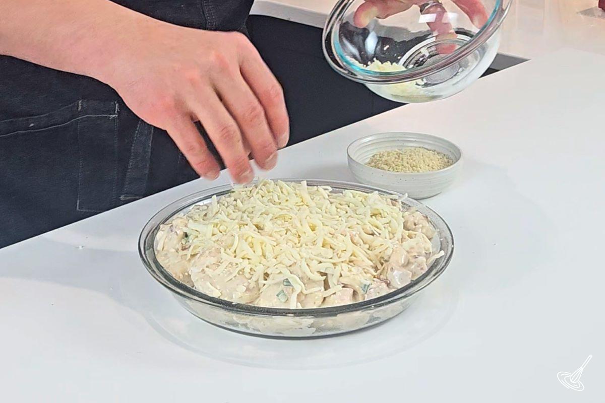 Someone sprinkling cheese over the Crack Chicken Pierogi Casserole before placing it in the oven.