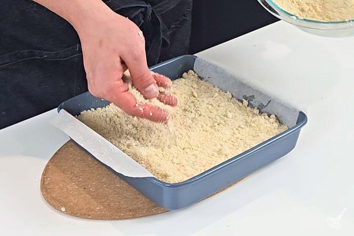 Someone sprinkling crumble mixture in a baking pan. 