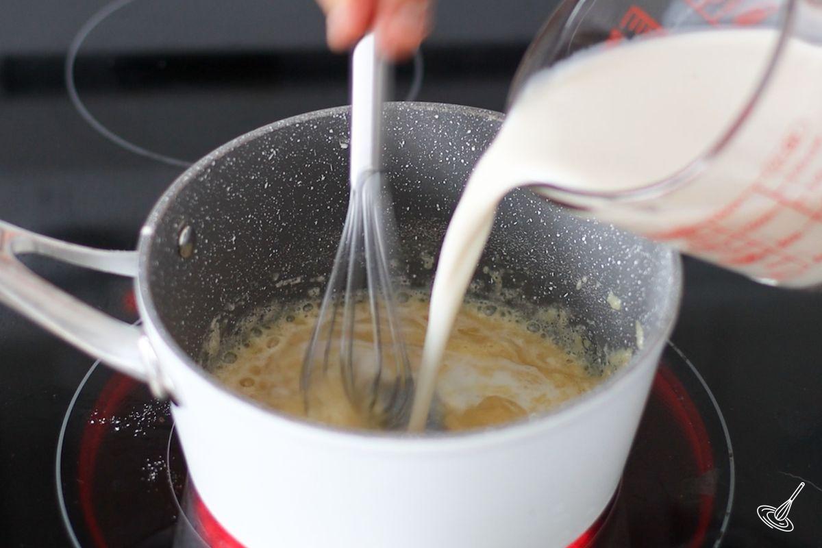 Someone pouring milk into a roux.