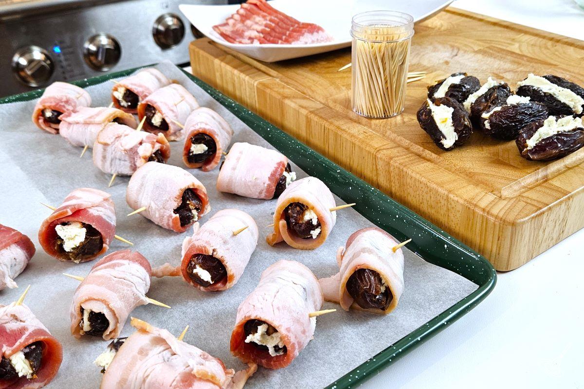 Dates Stuffed with Goat Cheese, wrapped in bacon, being placed on a baking tray.