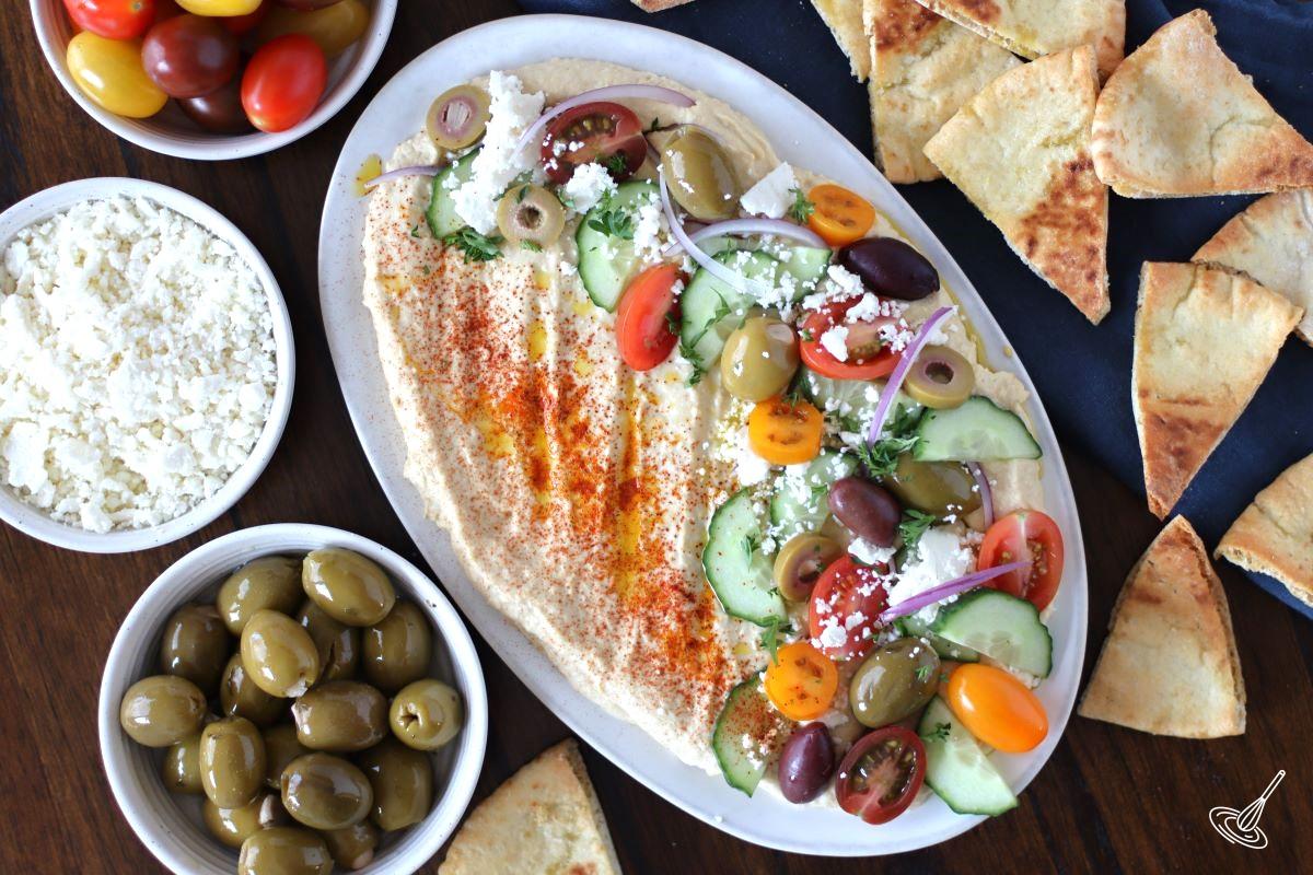 Greek Loaded Hummus with side bowls of feta, olives, tomatoes and pita chips.