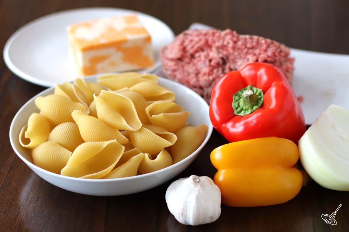 Ingredients to make stuffed shells including jumbo pasta shells, cheese, ground meat, and vegetables. 