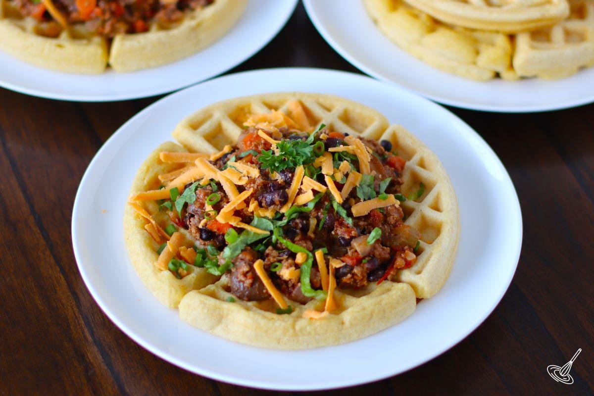 A cornbread waffle topped with chili on a plate. 