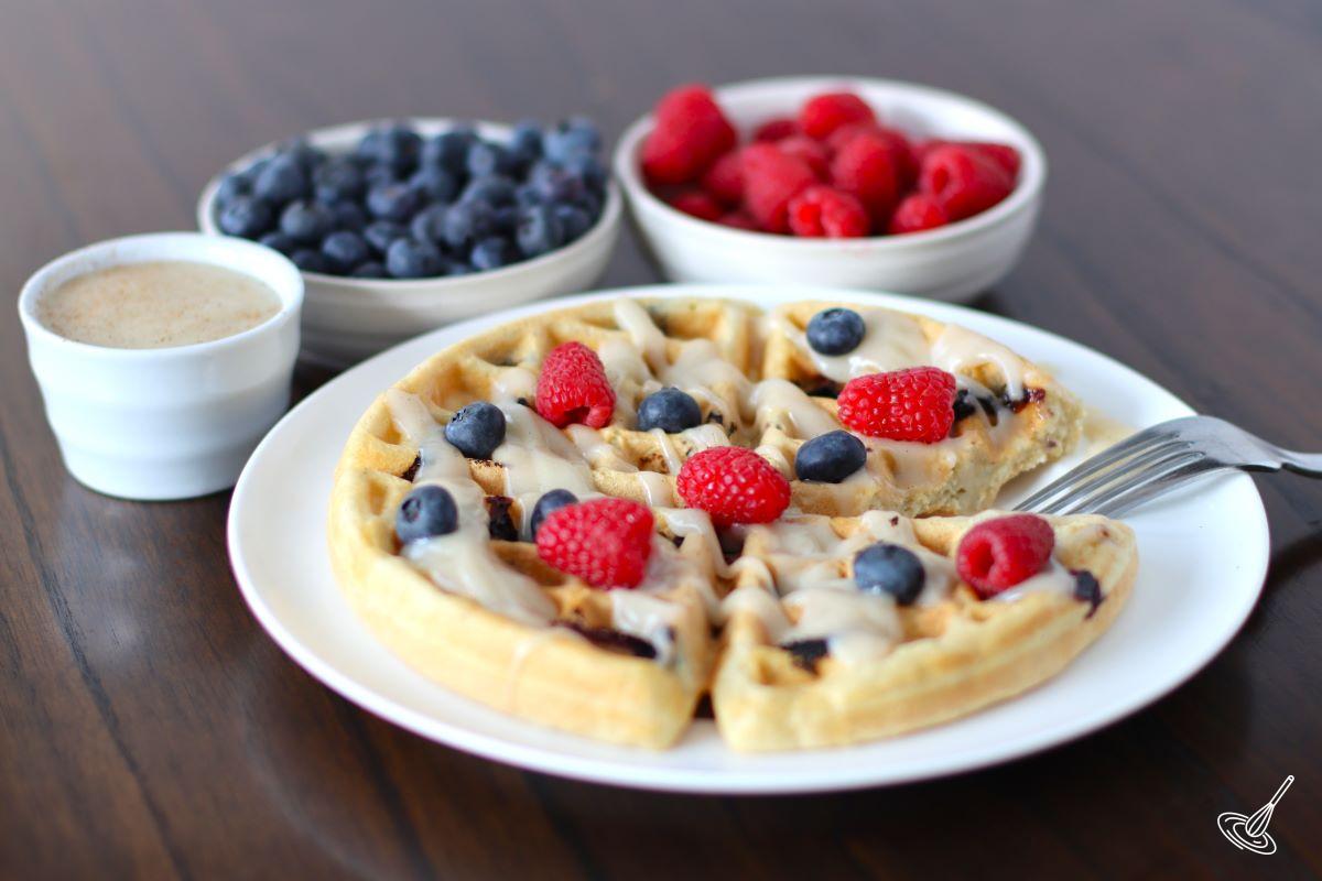 A plate of waffles with a side of berries and waffle sauce. 