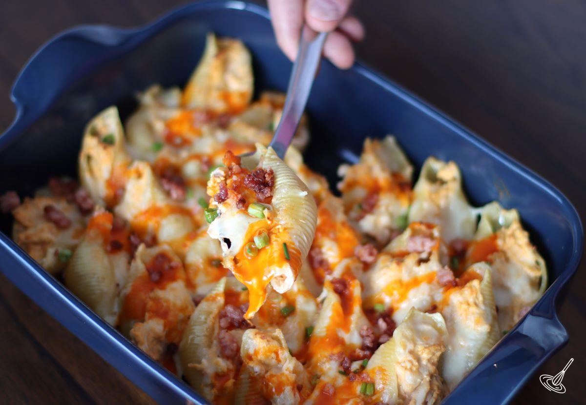 Someone taking a stuffed pasta shell with a spoon.