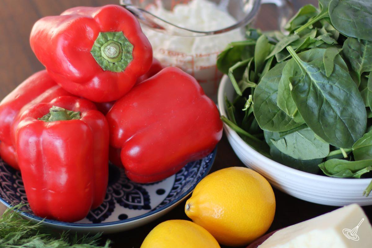 A bowl of red bell pepper with a bowl of fresh spinach beside it. 