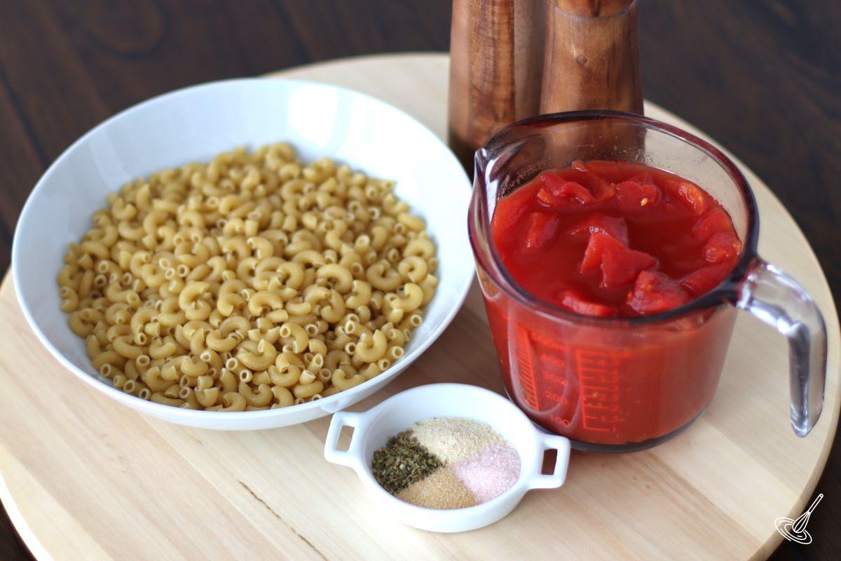 A picture of a bowl of raw elbow macaroni and a container of canned tomatoes. 
