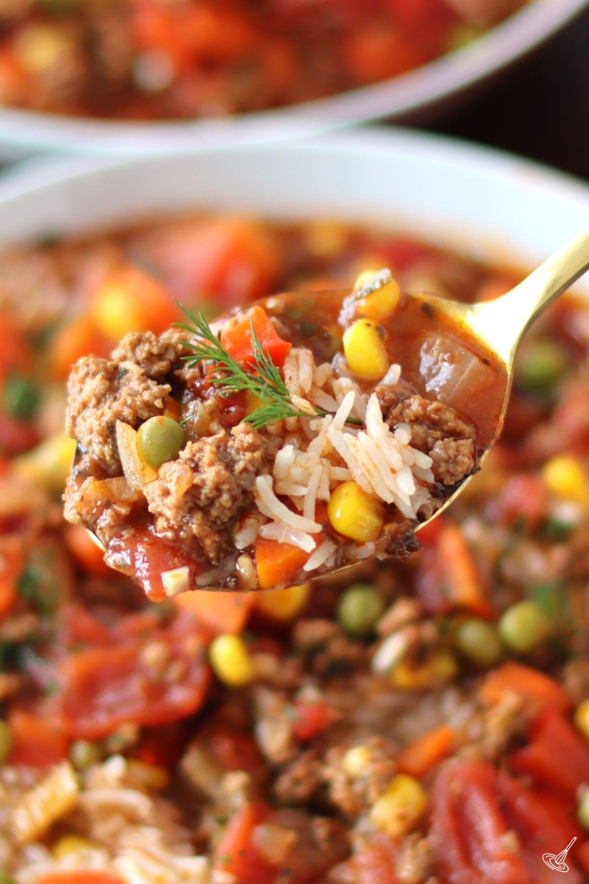 A spoonful of Beef and Rice Soup being held over the bowl of soup. 