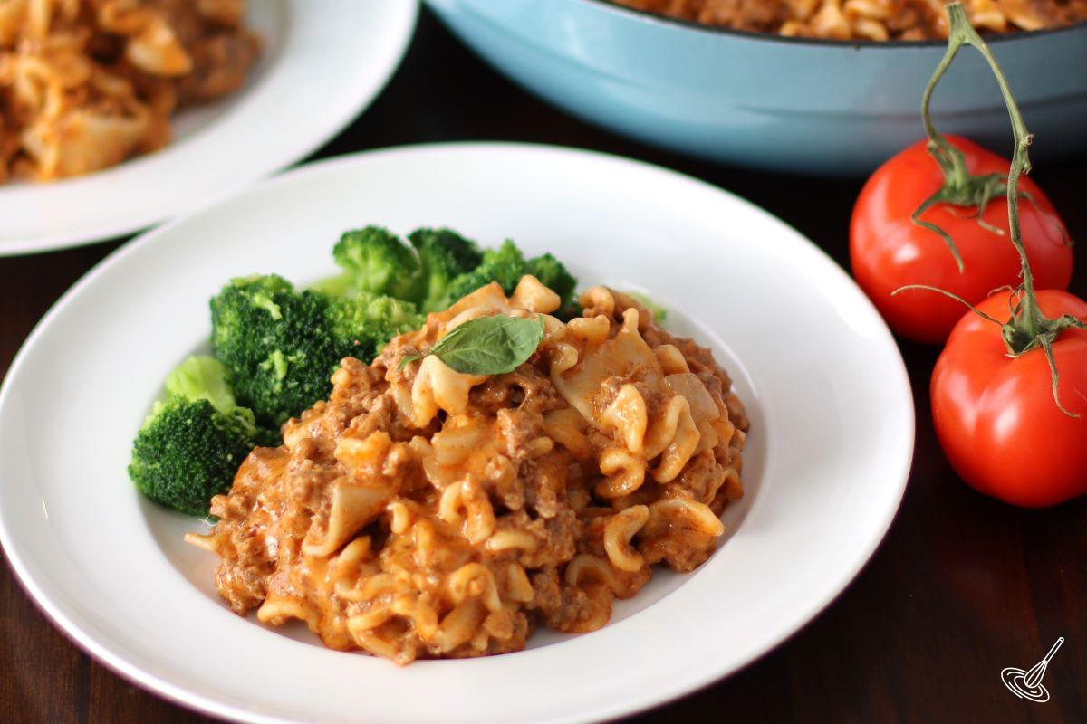 A portion of beefaroni recipe on a plate with a side of steamed broccoli.