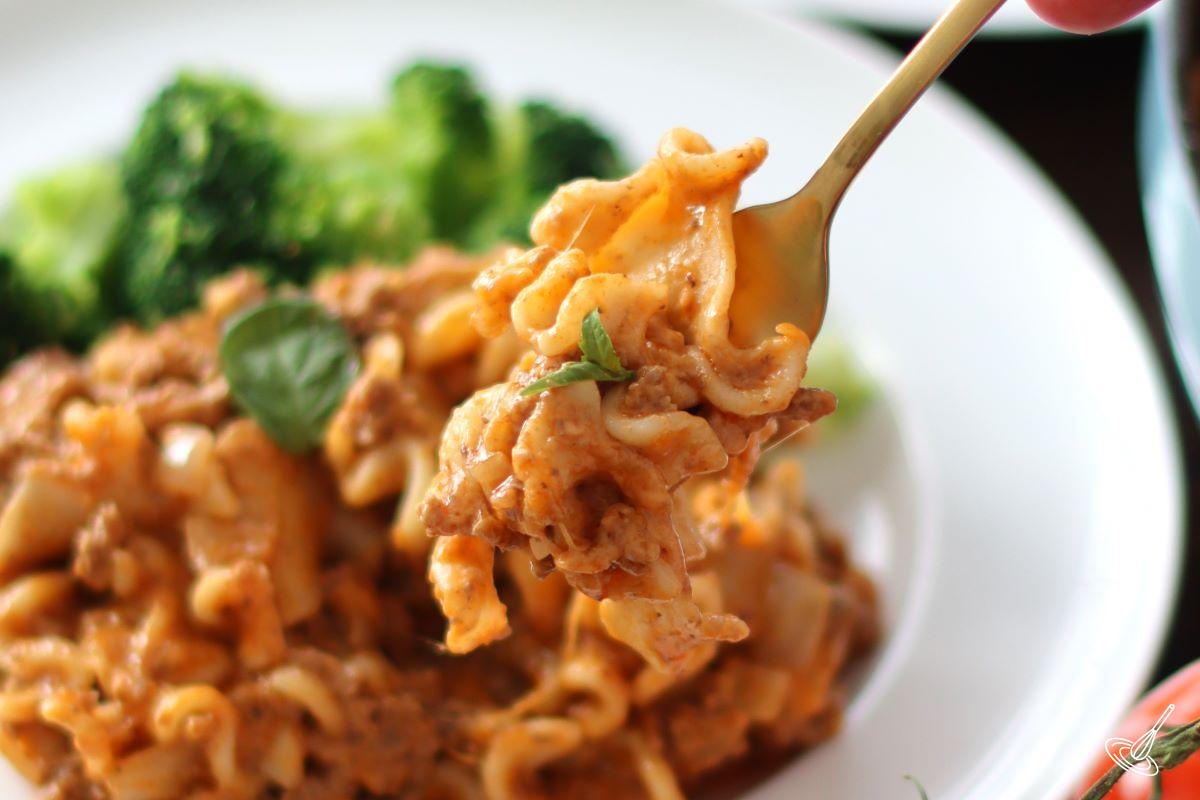 A fork holding pasta over a plate with broccoli. 