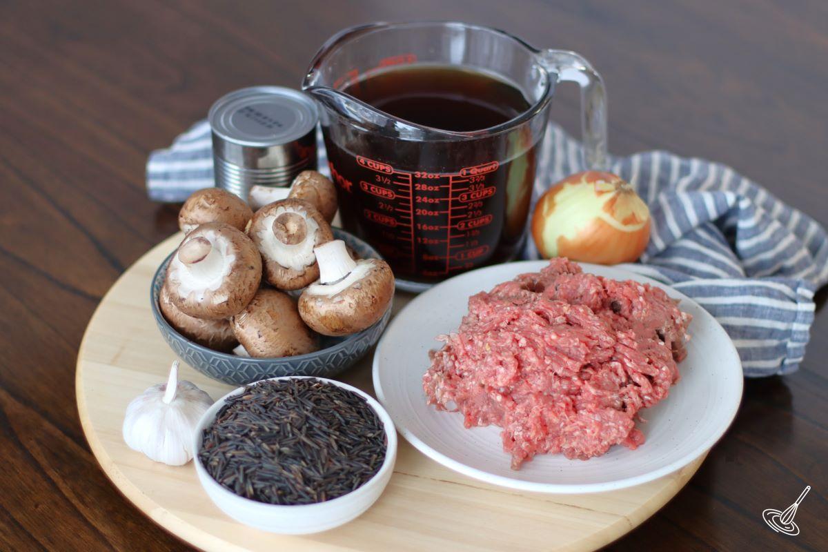 Ingredients on a table, including ground beef, wild rice, mushrooms and beef broth. 