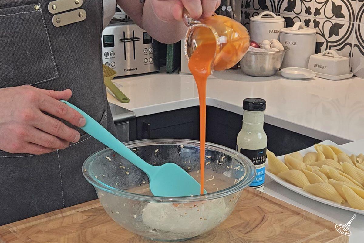 Someone pouring buffalo sauce in a large bowl with cream cheese. 