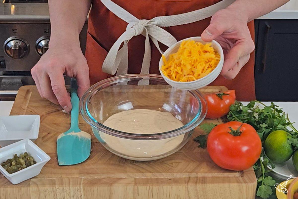 Someone placing grated cheddar cheese in a bowl with cottage cheese.