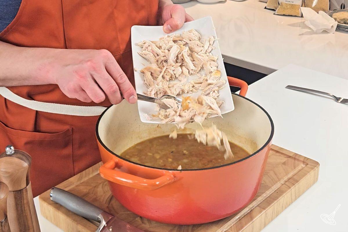 Someone adding shredded chicken into the Chicken Pastina Soup. 