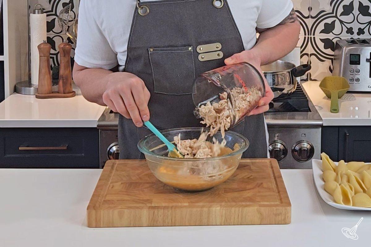 Someone placing shredded chicken in a large bowl with buffalo sauce and cream cheese. 