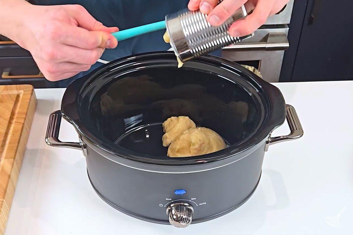 Someone pouring in a can of condensed cream of chicken soup into a slow cooker.