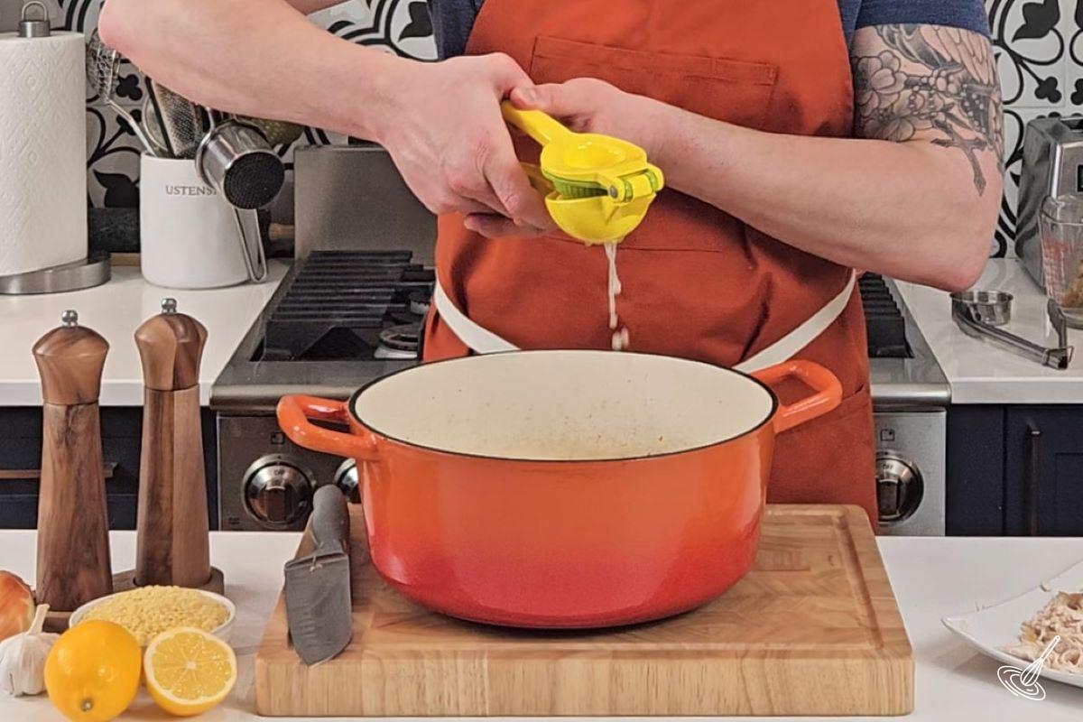 Someone using a lemon juicer and squeezing fresh lemon juice into a soup.
