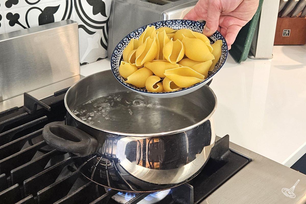 Someone putting jumbo pasta shells in a large pot of boiling water. 