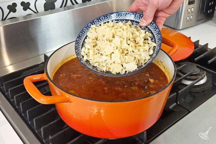 Someone adding lasagna pasta to a Dutch oven of soup. 