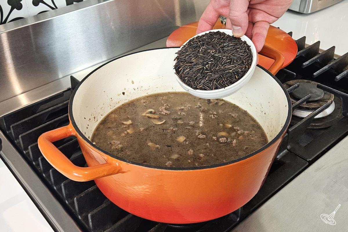 Someone adding wild rice to a soup.