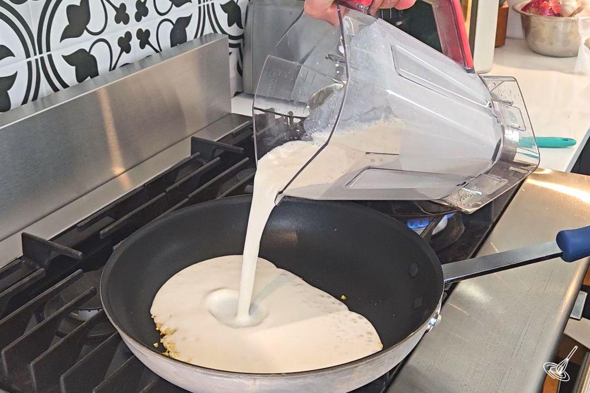 Someone pouring a white sauce in frying pan. 