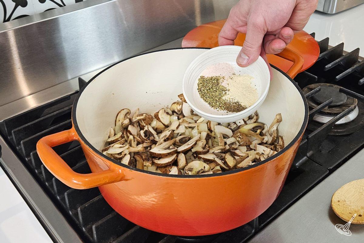 Someone adding sliced to a pan with mushrooms.