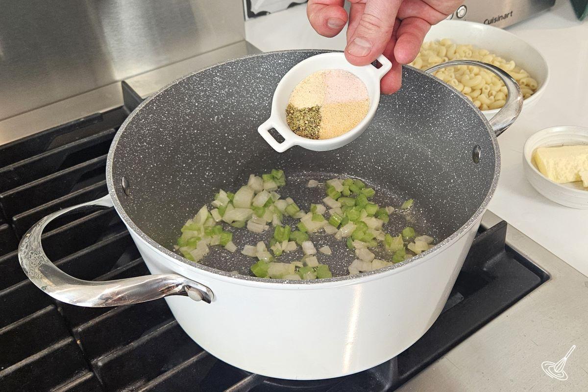 Someone adding a blend of spiced to a large pot with cooked onion and celery. 