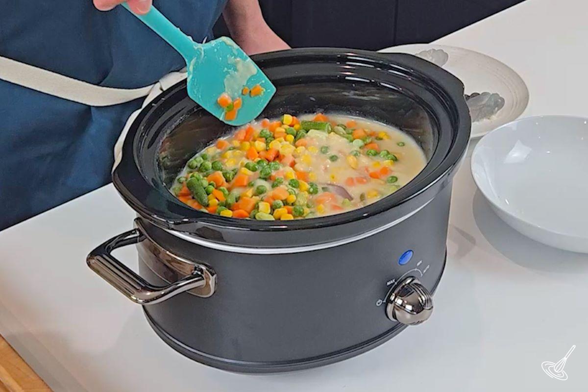 Someone stirring in vegetables into a slow cooker.