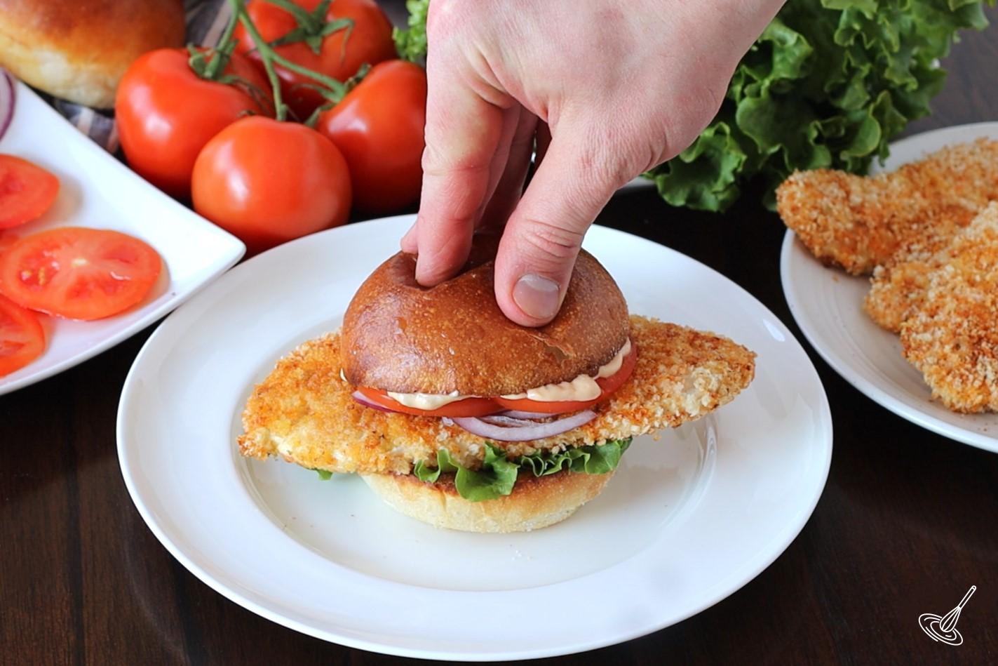 Someone placing the top bun on a Crispy Cajun Chicken Sandwich. 