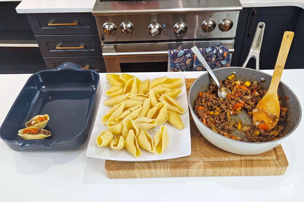A plate of cooked pasta shells with a pan of meat filling on the side. 