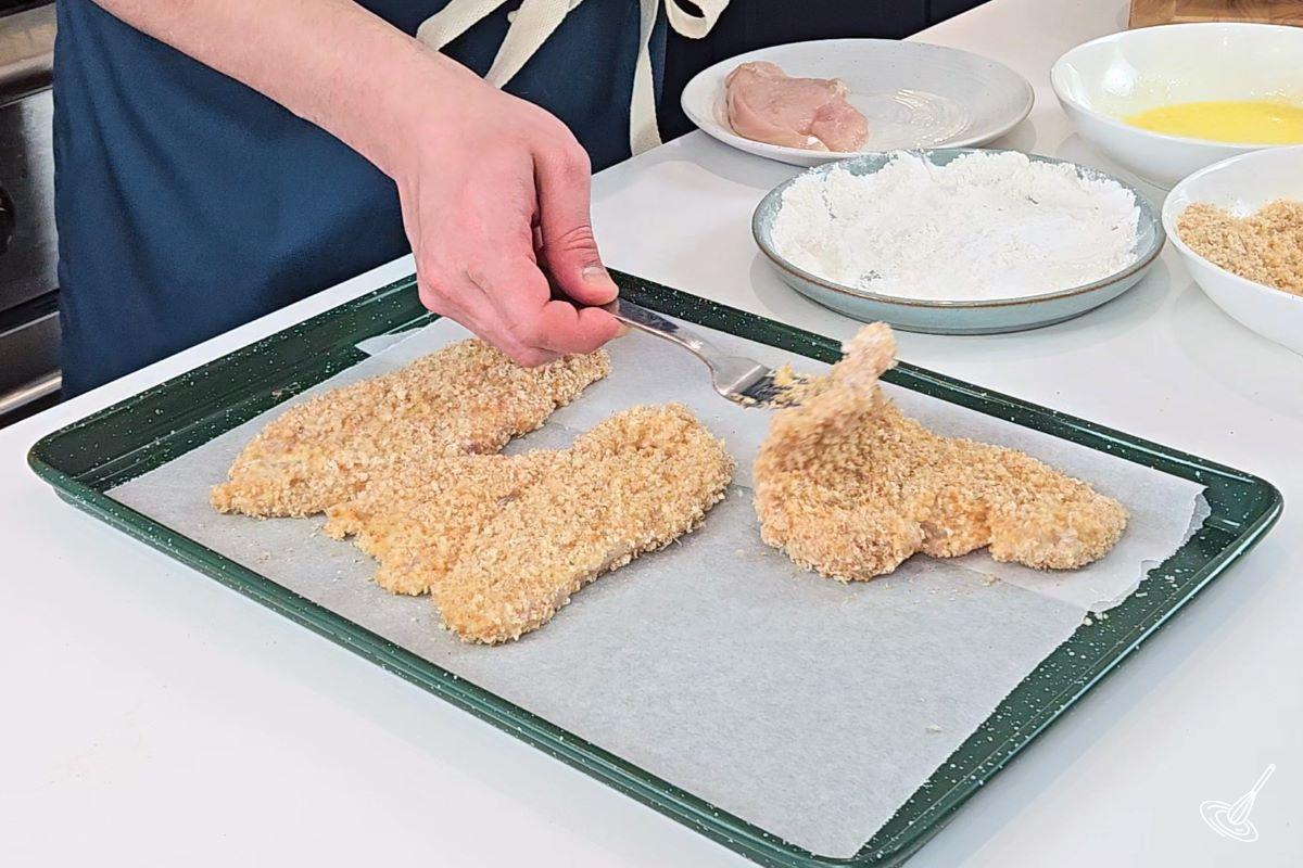 Someone placing coated chicken breast on a baking tray. 