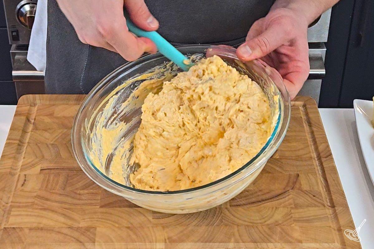 Someone stirring a buffalo chicken cream cheese mixture in a bowl. 