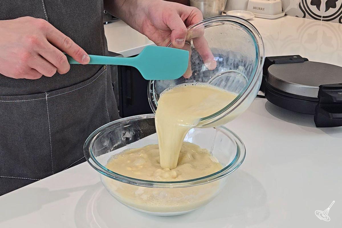 Someone pouring a bowl of liquid ingredients in a larger bowl of dry ingredients. 