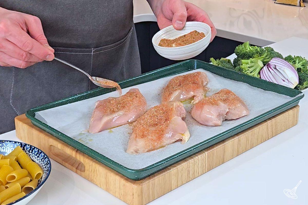 Someone sprinkling Cajun seasoning on raw chicken breasts.