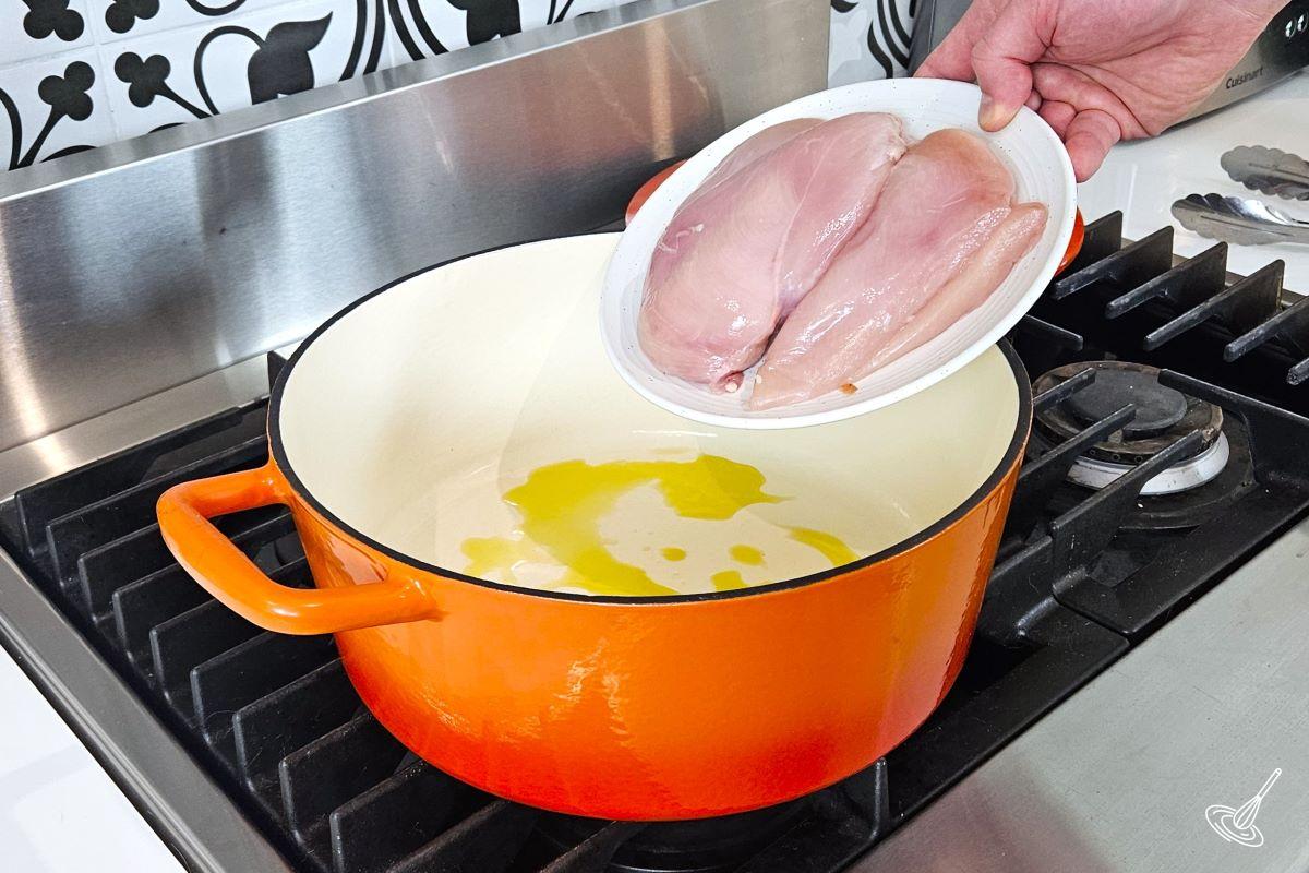 Someone placing chicken breasts in a Dutch oven which is on the stove. 